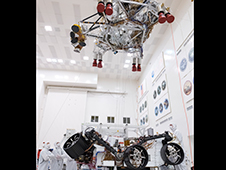 Employees look on as a crane lifts the rocket-powered descent stage away from the Mars 2020 rover