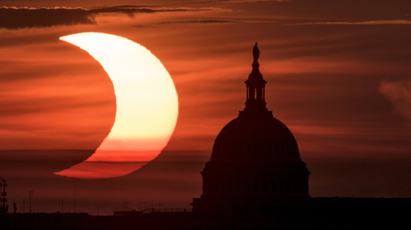 In this photo provided by NASA, a partial solar eclipse is seen as the sun rises to the left of the U.S. Capitol in Washington, Thursday, June 10, 2021, as seen from Arlington, Va.