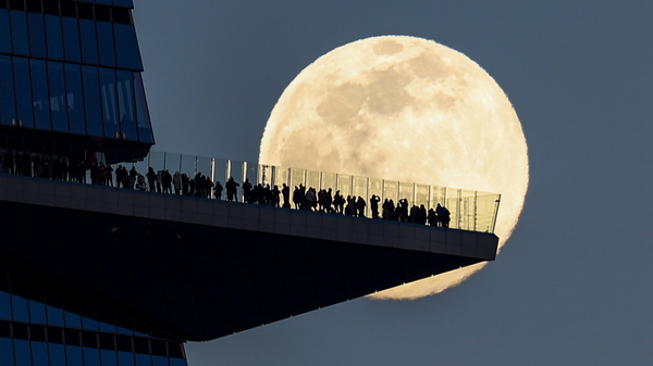 The moon rises on Tuesday behind people standing on The Edge, the outdoor observation deck in Manhattan.