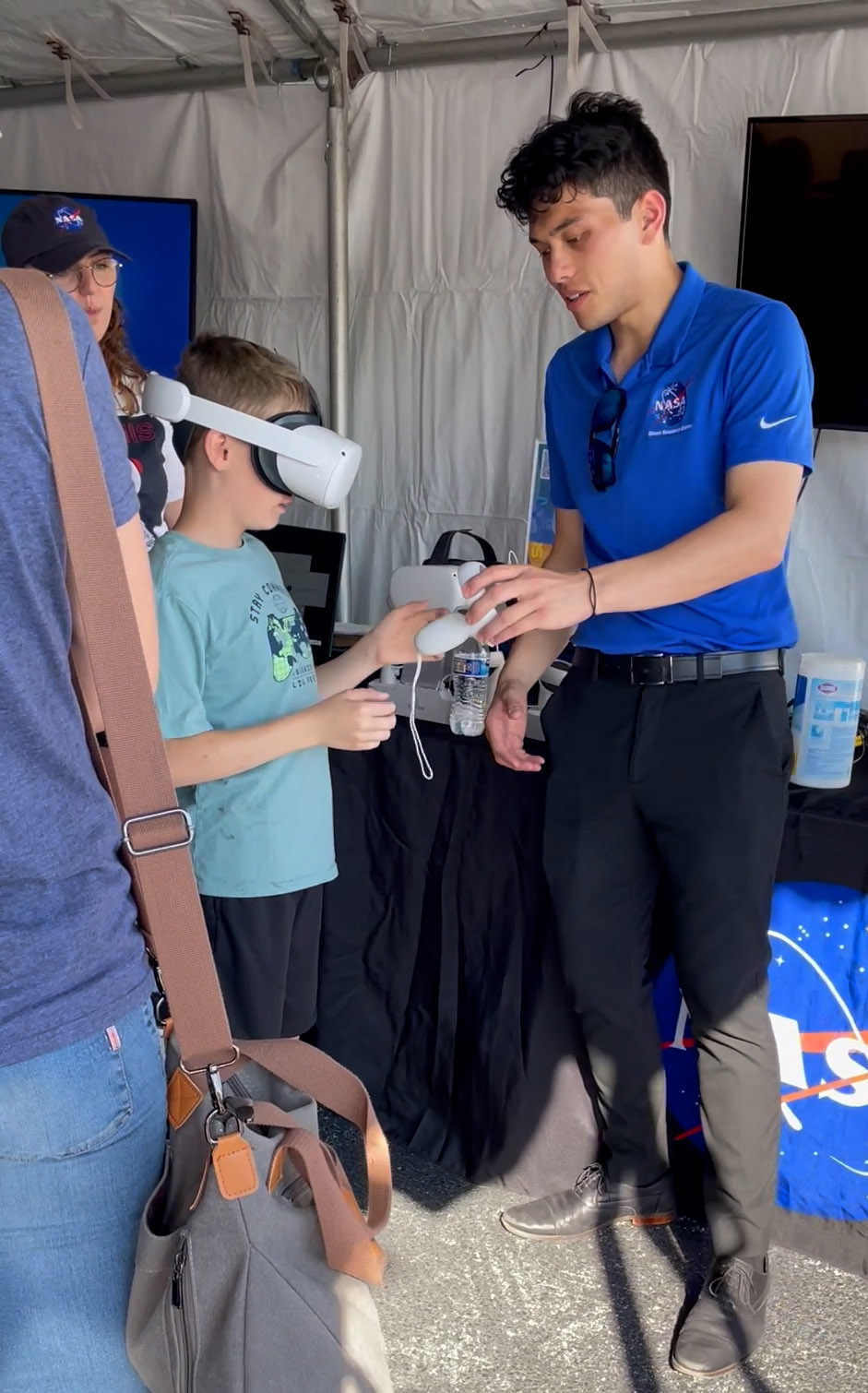 Mark Frances shows a young boy how to use his goggles and controls to experience interactive technology. They are inside a tent.